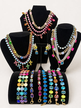 A black jewelry display stand filled with colorful beaded and rhinestone bracelets and rings, photographed in a store setting with a blurred background.