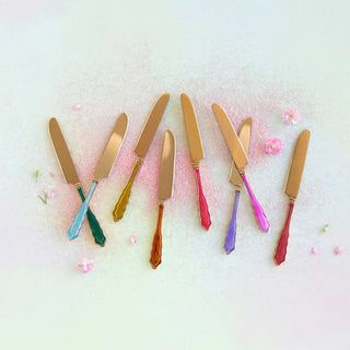 Set of colorful knives on a textured white surface with pink floral elements.