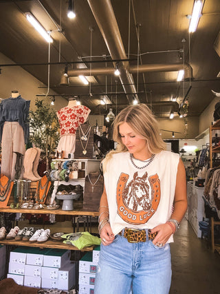 Woman in a store wearing a white sleeveless top with a horse graphic and blue jeans.