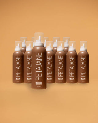 A group of PETAJANE hair product bottles arranged in a fan shape against a solid warm tan background. The bottles are brown with white caps and white vertical branding text.
