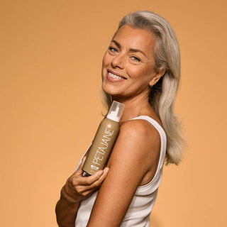 Woman holding a bottle of Petalane product against an orange background