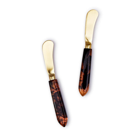 Two butter knives with tortoiseshell handles and gold blades on a white background