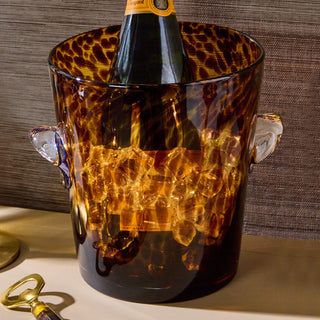 Bottle of champagne in a leopard print ice bucket on a wooden surface. Tortoise shell ice bucket.