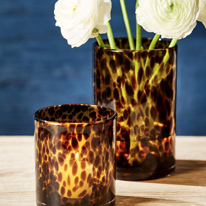 Two tortoiseshell patterned glass vases with white flowers against a blue background