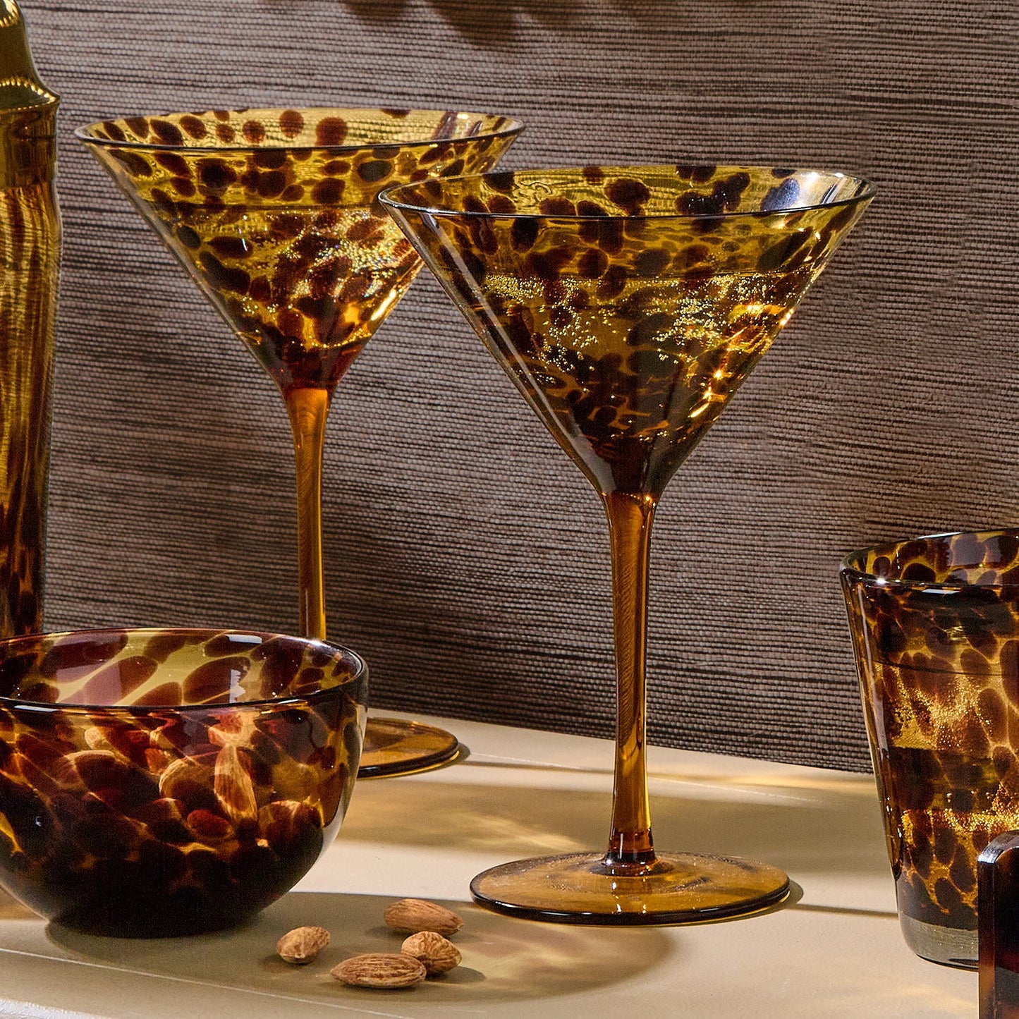Leopard print glassware including martini glasses and a bowl on a textured surface. Tortoise shell martini glasses