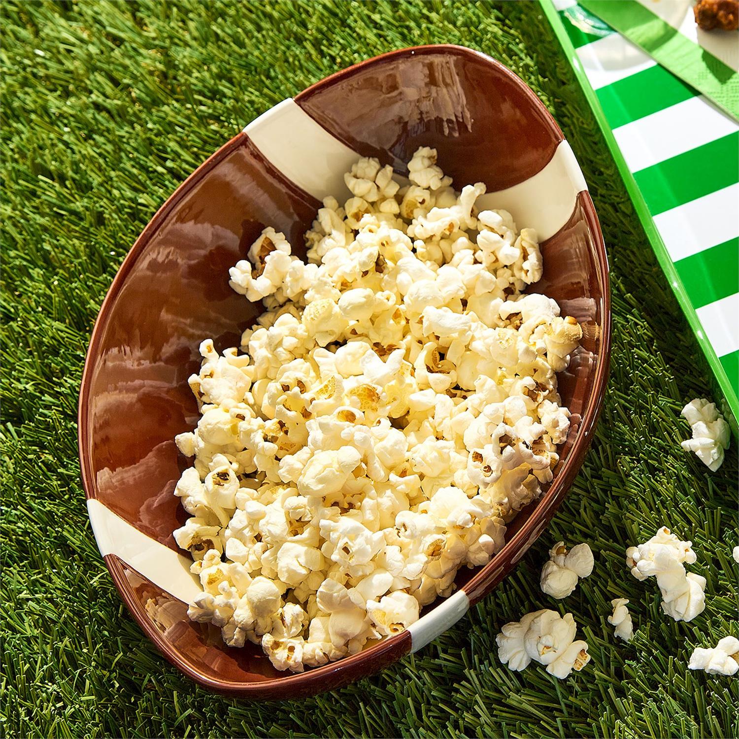 Brown football-shaped bowl filled with popcorn on a grassy field