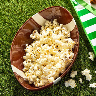 Brown football-shaped bowl filled with popcorn on a grassy field