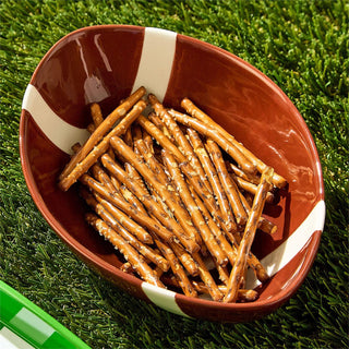 Football-shaped bowl filled with pretzel sticks on a grassy background