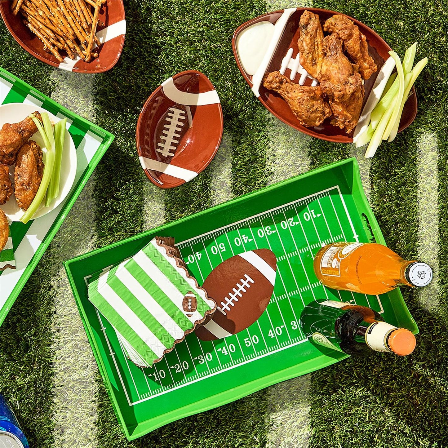 Football-themed snack platter with wings, fries, and a bottle of beer on a grass-like surface.