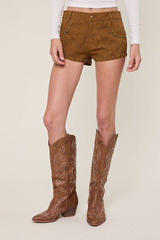 Person wearing brown suede shorts with gold studs and brown cowboy boots on a beige background
