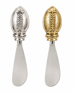 Two metal cheese knives with football-shaped handles, one in silver and one in gold, shown side by side on a white background.
