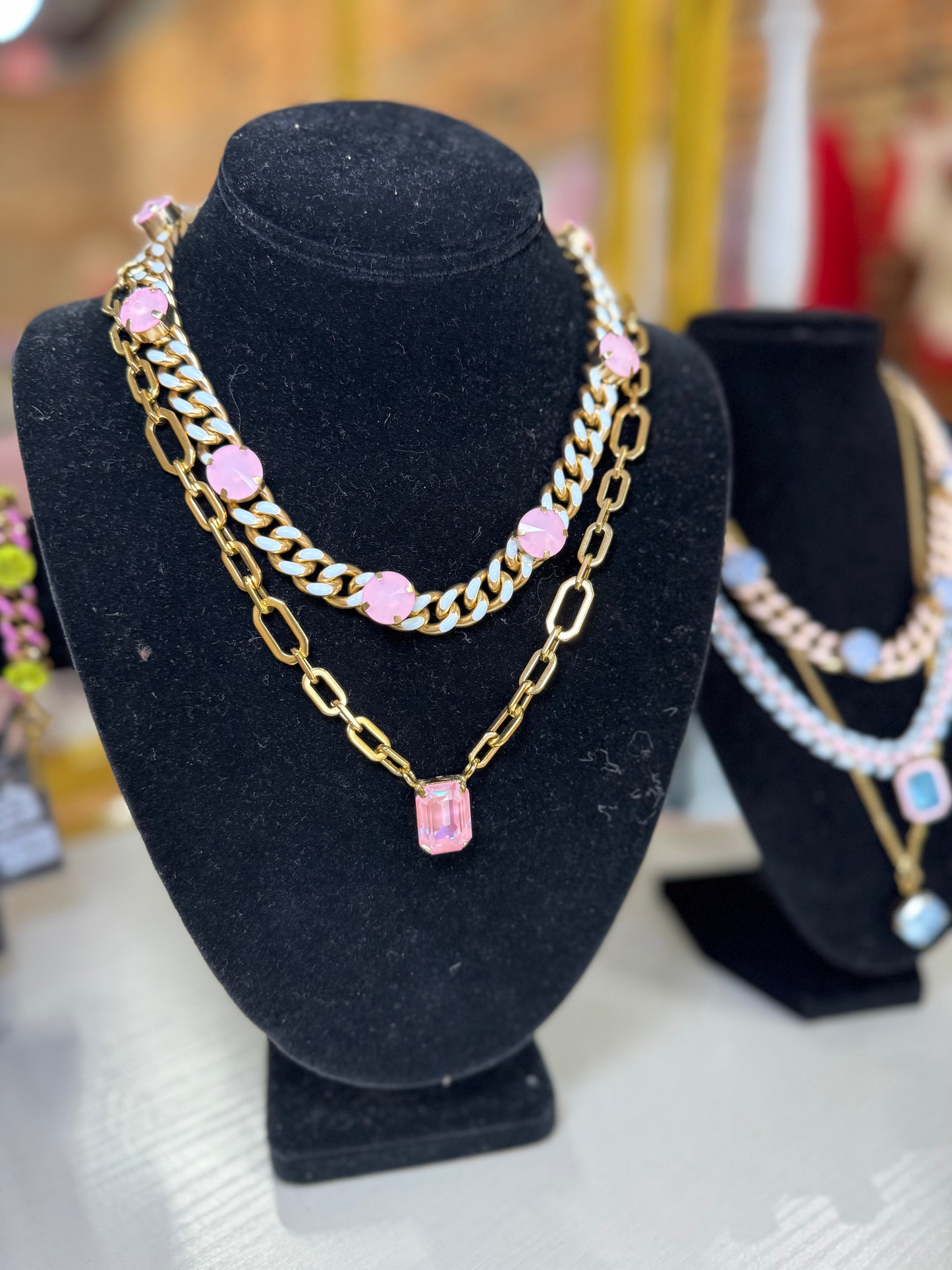 A gold-toned chunky chain necklace with pink gemstone accents and a rectangular pink pendant, displayed on a black velvet jewelry bust.