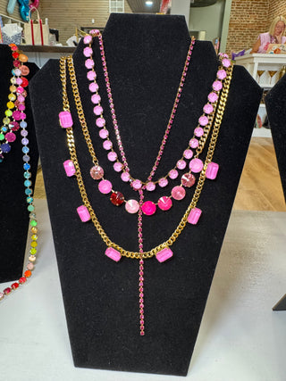 A multi-layered necklace displayed on a black velvet jewelry bust. The necklace features gold-tone and pink-tone chains with pink faceted beads and stones in round, oval, and rectangular shapes.