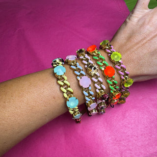 A set of five chunky gold-tone chain bracelets with colorful faux gemstones, worn stacked on a person's wrist against a bright pink background.