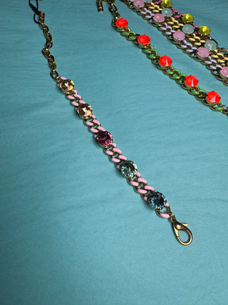 A handmade chain link bracelet with pink braided cord and colorful faceted rhinestones, displayed on a turquoise background alongside other bracelets.