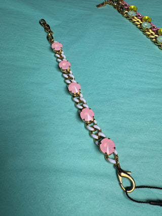 A gold-tone chain bracelet with alternating pink and white oval beads, displayed diagonally on a teal fabric background.