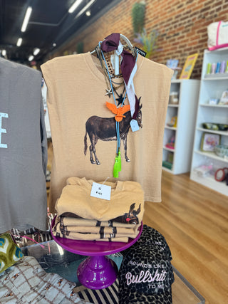 A tan graphic t-shirt featuring a donkey illustration and a colorful butterfly ornament, displayed on a hanger on a store shelf next to folded matching t-shirts.
