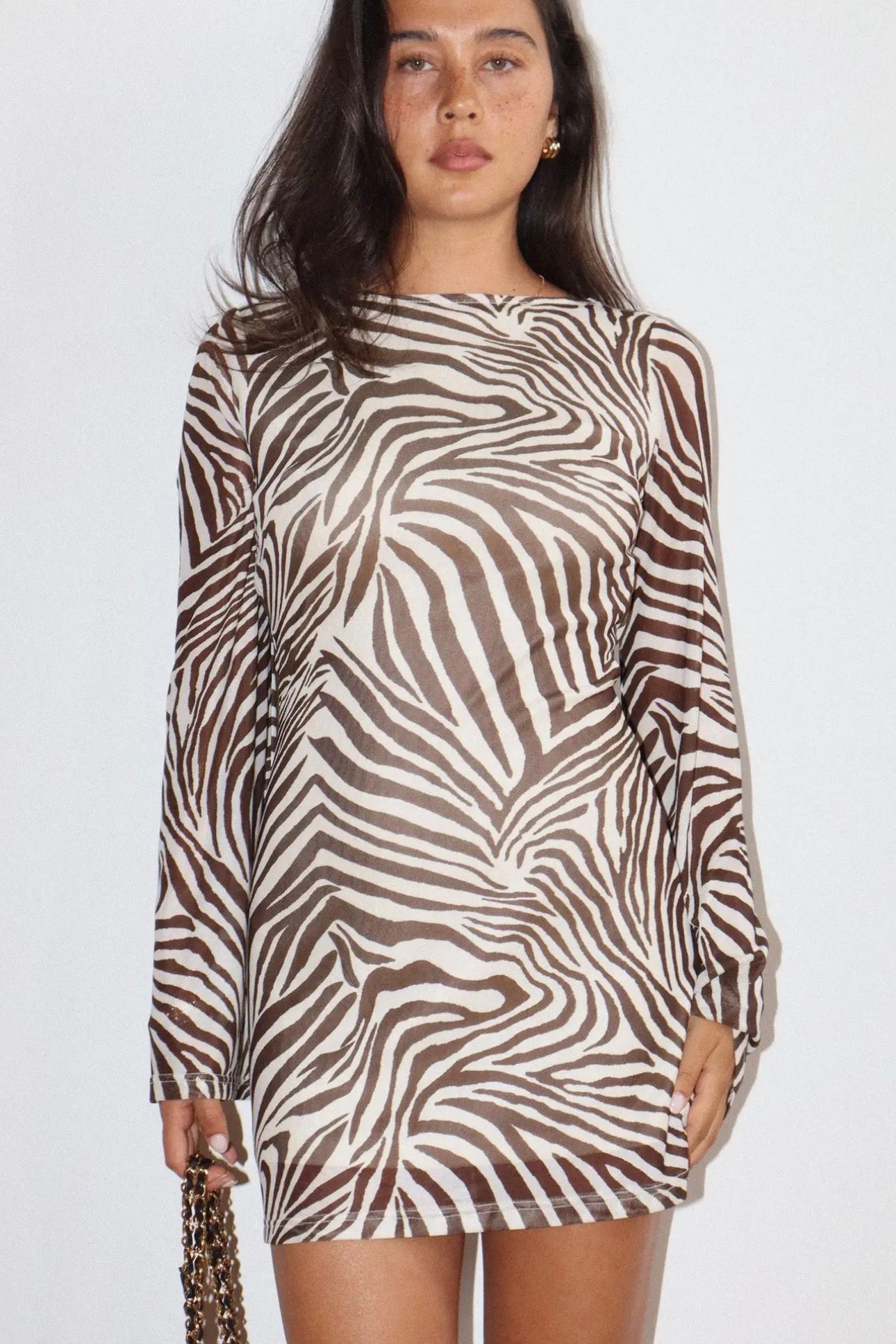A woman wearing a long-sleeve mini dress with a brown and beige zebra print, standing against a plain light gray background.
