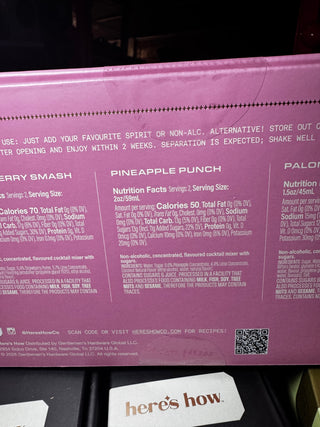 Close-up of the back of a pink beverage box showing flavor labels and nutrition facts, with a small card reading 'here's how.' visible at the bottom.