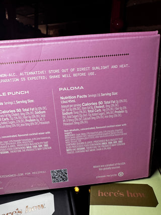 A close-up of a purple Palau cocktail mixer box showing the back panel with nutrition facts and usage text, with a small card reading 'here's how' partially visible at the bottom.