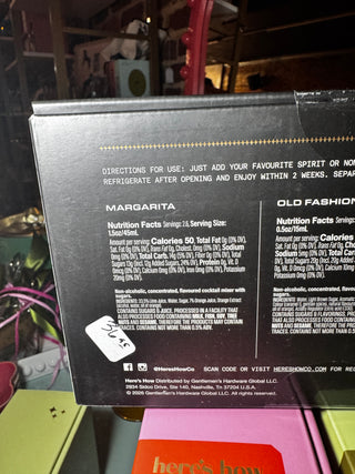The back of a black Her's How box showing product details, nutrition facts, and directions for use for a Margarita cocktail, with a white handwritten price sticker on the side.