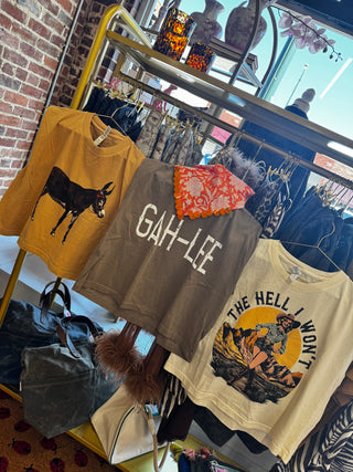 Three graphic crewneck sweatshirts hanging on a gold clothing rack in a retail store. The left sweatshirt is mustard yellow with a black donkey graphic.