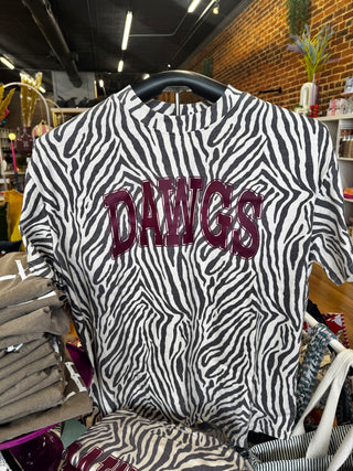 A zebra-print short-sleeve t-shirt with 'DAWGS' printed across the chest in a dark burgundy collegiate font, hanging on a black hanger in a retail store.