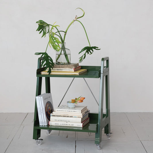 Green metal cart with books and a plant on a light gray floor.