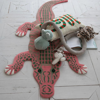 Pink alligator-shaped rug with plush toys on a light wooden floor
