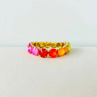 A gold-plated stretch band bracelet featuring a gradient of colorful oval cabochon gemstones transitioning from pink and red to orange, yellow, and lime green, displayed on a neutral light gray background.