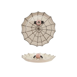 A ceramic spiderweb-themed dish with a scalloped rim, featuring a top-down view of a spiderweb pattern with a pink center and a bottom view showing a small raised spider face at the hub.