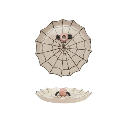 A ceramic spiderweb-themed dish with a scalloped rim, featuring a top-down view of a spiderweb pattern with a pink center and a bottom view showing a small raised spider face at the hub.