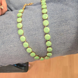 A gold-tone chain necklace with round light green faceted beads draped over blue denim fabric.