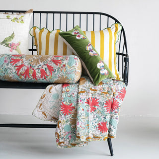 Floral quilt and pillows on a black metal bench against a white background