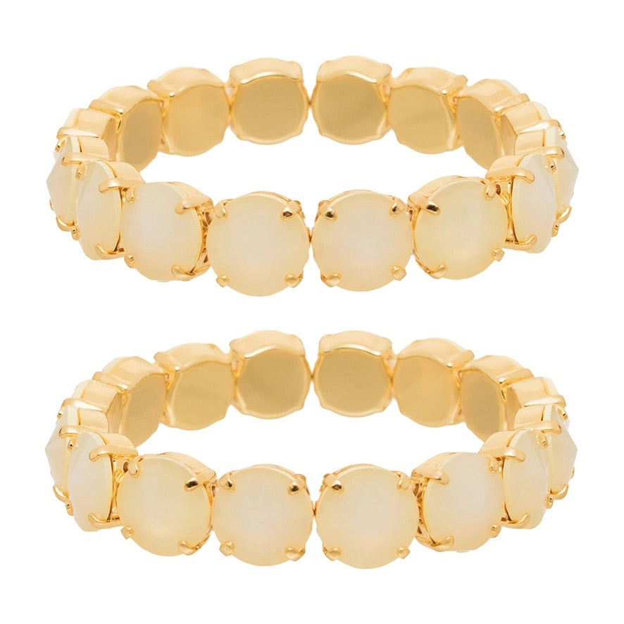 Two gold-plated stretch bands, each featuring a row of round, dome-shaped cream-colored cabochon gemstones, displayed against a solid white background.