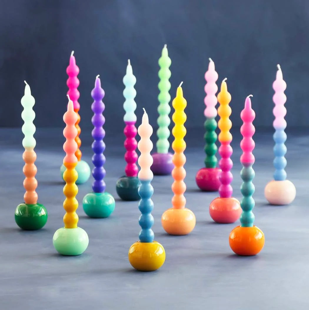 A set of colorful spiral candles with rounded, bead-like segments and solid-colored bases, arranged on a dark gray surface against a dark blue-gray background.