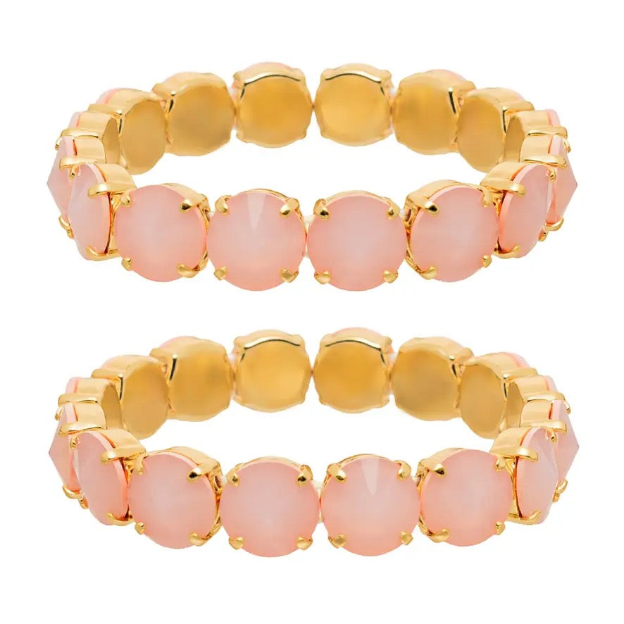 Two matching gold-plated stretch bracelets, each featuring a row of round, pale pink cabochon gemstones in prong settings, shown against a plain white background.