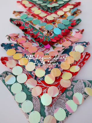 A pack of triangular scarf-shaped pieces covered with round reflective sequins on a white background, with layered floral and patterned fabrics underneath and the text 'O2 Sequin Scarf Pack Two' across the center.