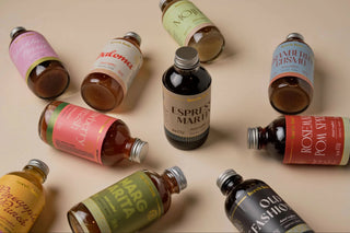 A styled flat-lay arrangement of multiple artisanal whiskey bottles with colorful labels, set against a solid beige background.
