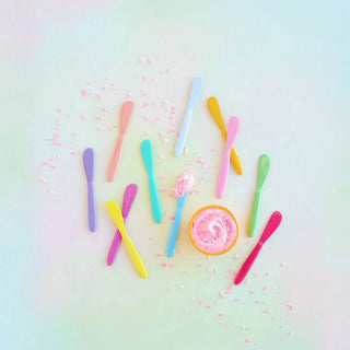 Colorful enamel metal spreaders in various vibrant solid colors arranged on a pastel background.