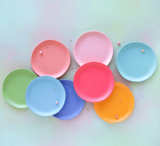 A collection of colorful melamine platters in pink, blue, green, yellow, and orange displayed on a pastel background.