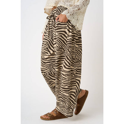 Zebra print pants worn with a white lace top on a plain background