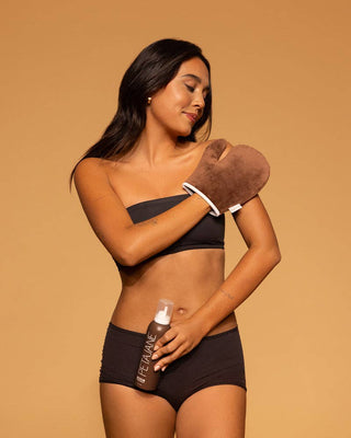 Woman wearing a black bikini holding a spray bottle against a beige background